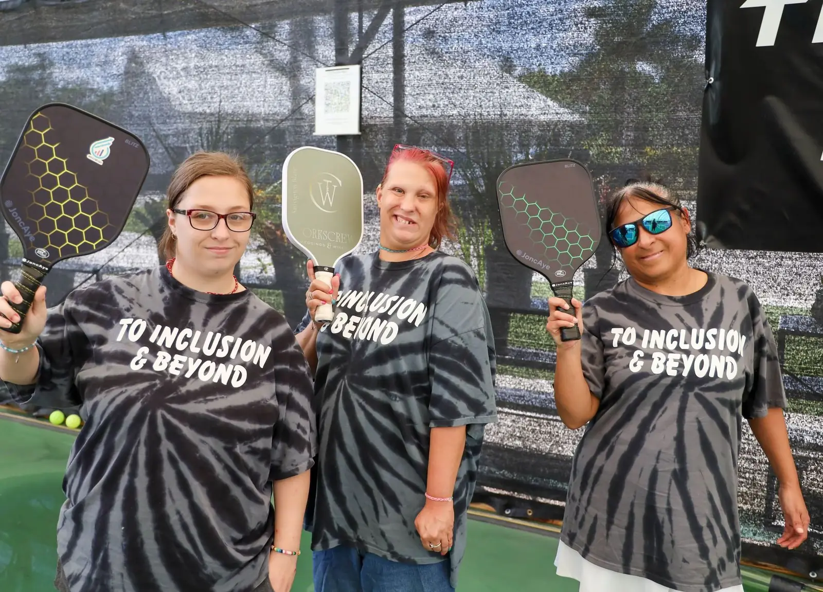 Three Ascend Transition Services members smiling and holding pickleball paddles at a community event
